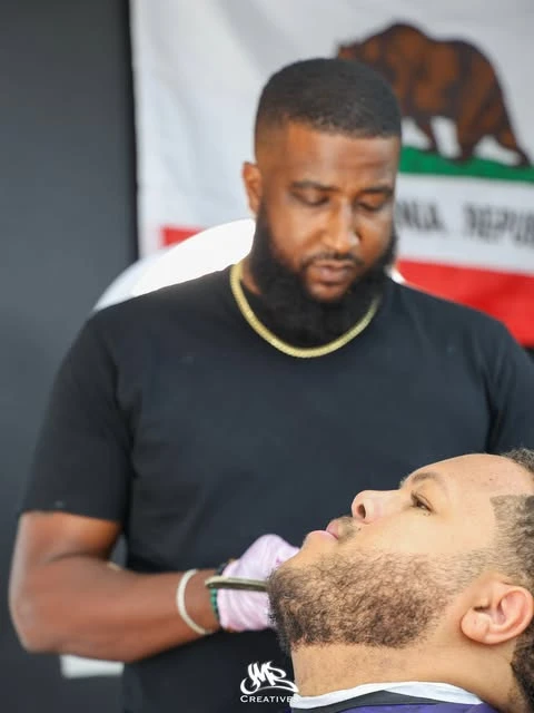 A barber carefully shaping a client’s beard at West Coast Barbershop