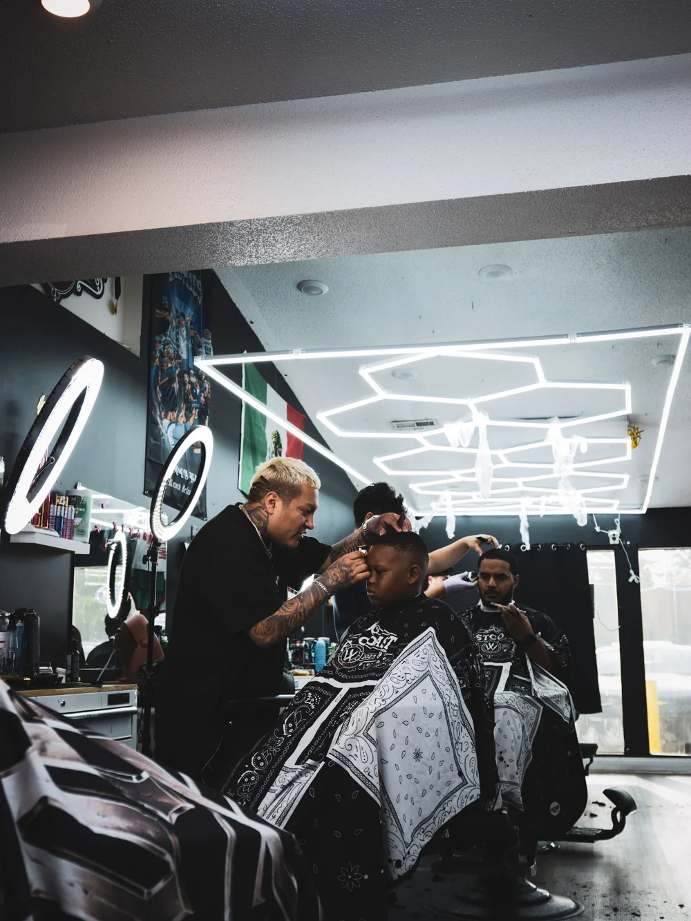 A West Coast barber working on a haircut beneath the shop’s geometric lighting